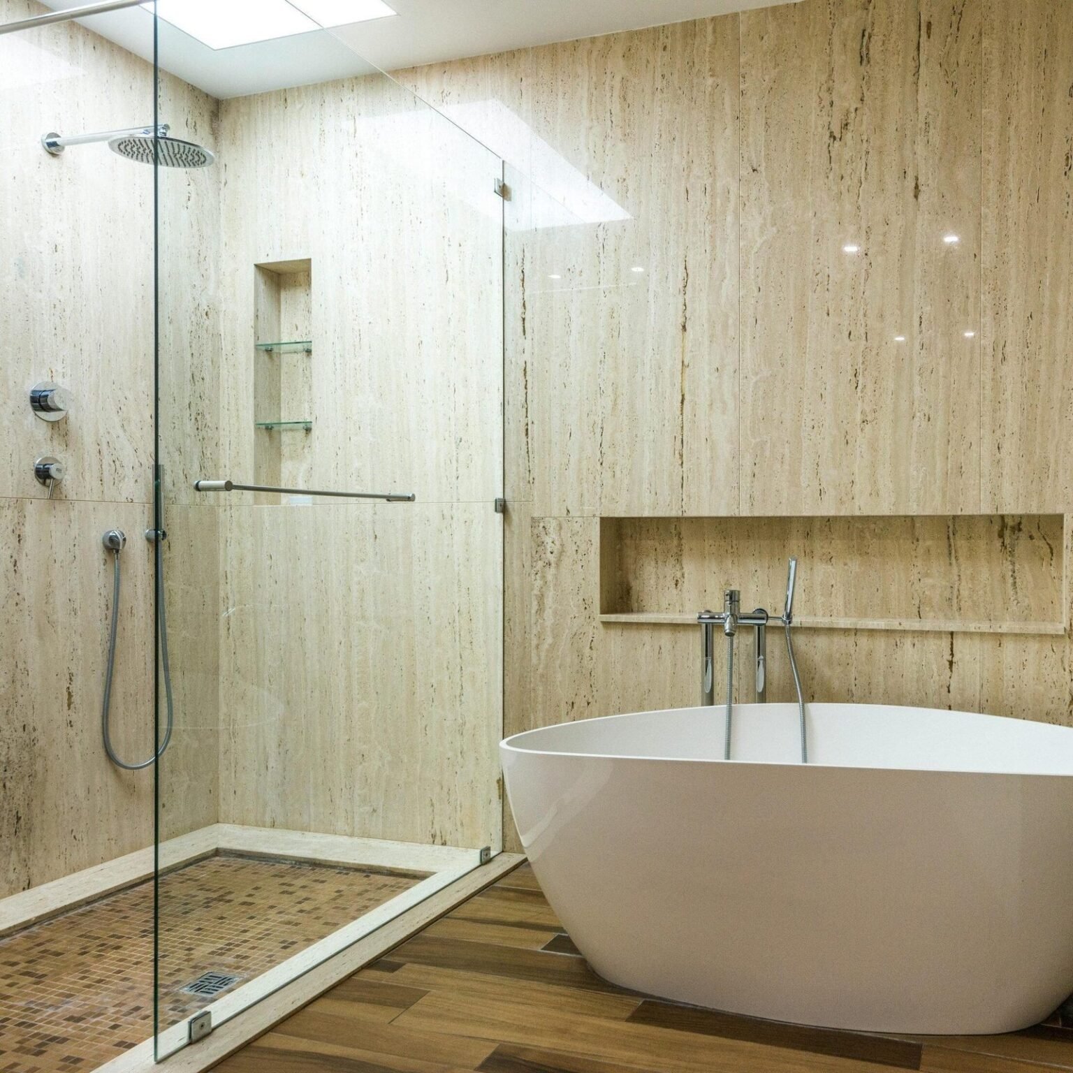 Baño con paredes de travertino, ducha acristalada, hornacina y bañera exenta