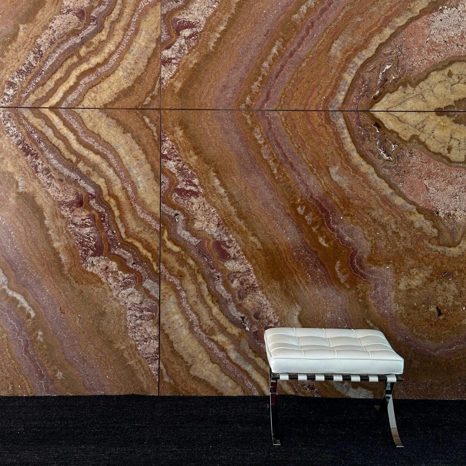 Pared revestida con grandes placas de travertino rojo de vetas onduladas y una banqueta blanca